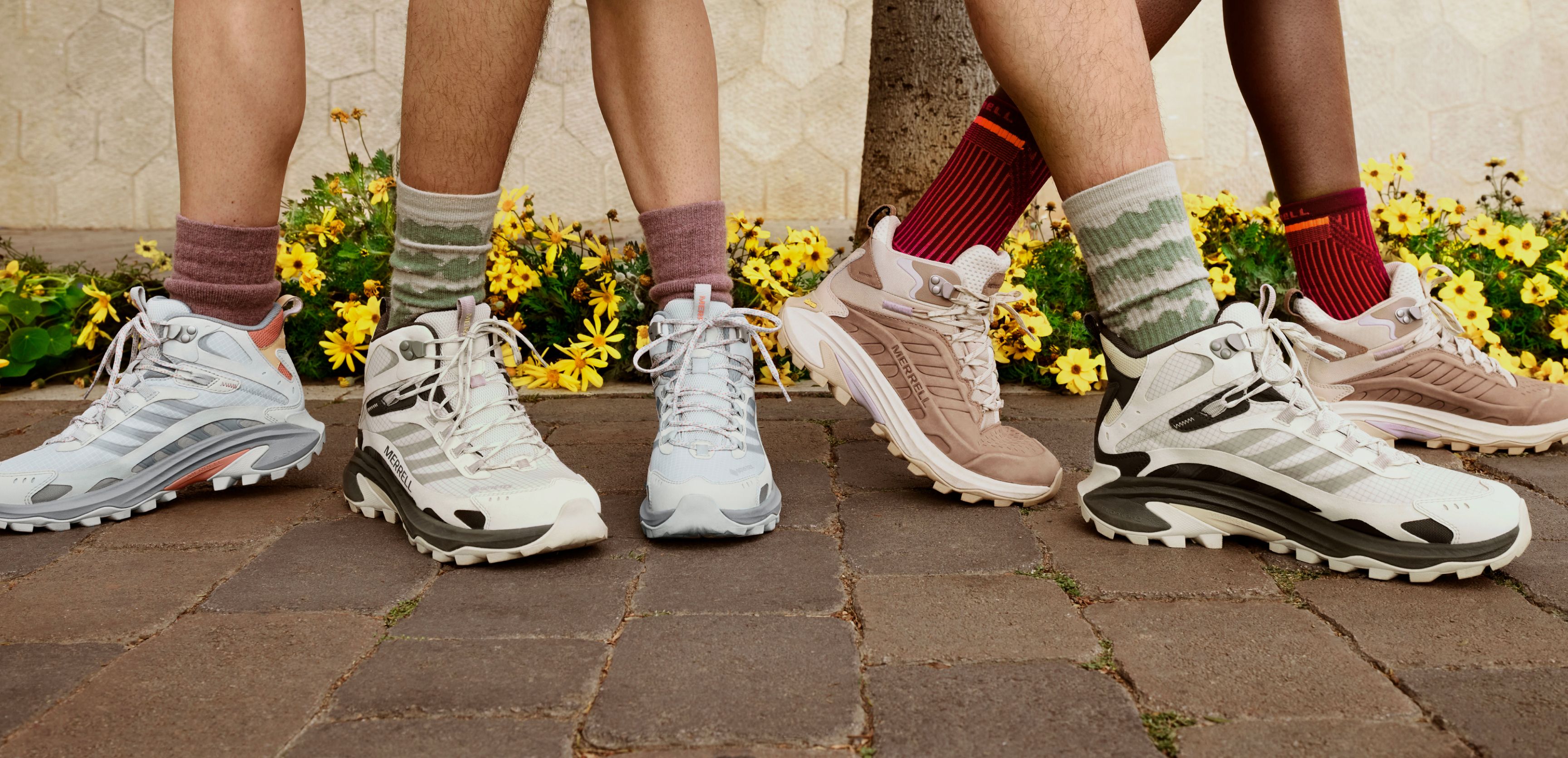 Three people wearing different Merrell Moab Speed 2 shoes standing on a brick path with yellow flowers in the background.